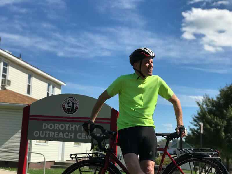 Brother Shamus McGrenra posing with bike at Dorothy Day Outreach Center Center