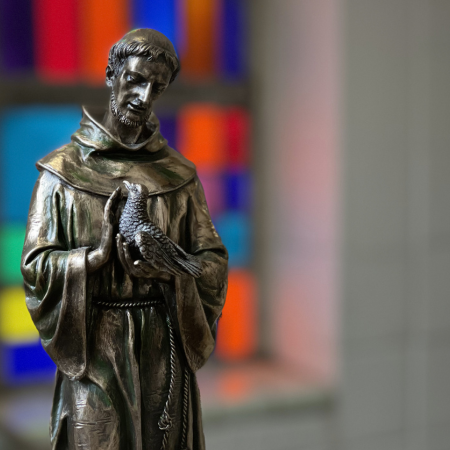 Small Bronze St. Francis Statue in front of Stained Glass